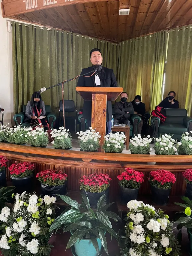 Speaker addressing the audience from a podium decorated with red and white flowers